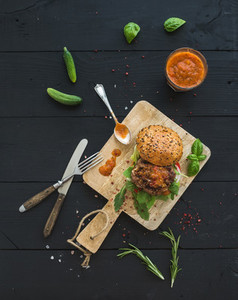 Fresh homemade burger on dark serving board with spicy tomato sauce  sea salt and herbs over black wooden background  Top view