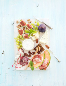 Wine snack set Figs grapes nuts cheese variety meat appetizers and herbs on light blue background top view