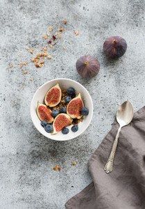 Healthy breakfast Bowl of oat granola with yogurt fresh blueberries and figs over grunge grey backdrop