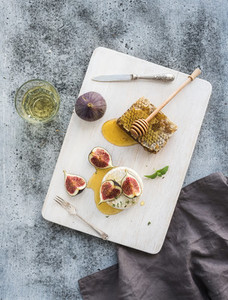 Camembert or brie cheese with fresh figs  honeycomb and glass of white wine on serving board over grunge rustic grey backdrop