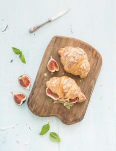 Freshly baked croissants with fresh figs and prosciutto on serving board over blue rustic wooden backdrop