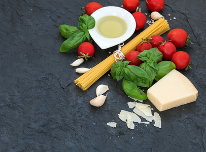 Ingredients for cooking pasta  Spaghetti  olive oil  garlic  Parmesan cheese  tomatoes and fresh basil on black slate background  top view  copy space