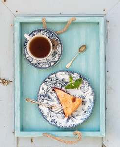 Piece of double crust plum pie and black tea in vintage porcelain cup  blue wooden tray  Top view