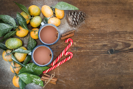 Christmas or New Year frame  Fresh mandarins with leaves  cinnamon sticks  pine cone  hot chocolate in mugs and candy canes over rustic wooden background  top view