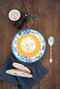 Homemade pumpkin cream soup in porcelain plate with spices and fresh bread slices on over rustic wooden background