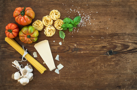 Ingredients for cooking pasta  Spaghetti  tagliatelle  garlic  Parmesan cheese  tomatoes and fresh basil on rustic wooden background  top view  copy space