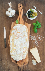 Freshly baked ciabatta bread with garlic  mediterranean olives  basil and Parmesan cheese on serving board over rustic wooden background