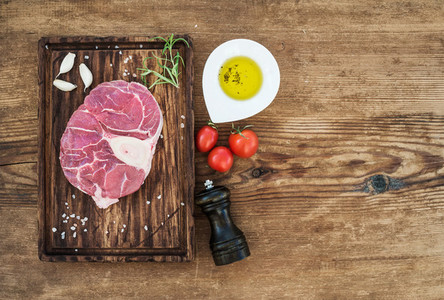 Raw fresh beef meat cross cut for ossobuco with garlic cloves  cherry tomatoes  rosemary  pepper  oil and salt on serving board over rustic wooden background