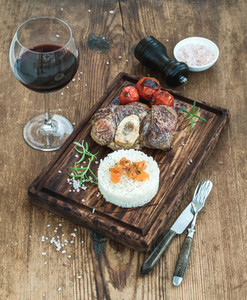 Roast beef Ossobuco with rice  vegetables and glass of wine on serving board over rustic wood background