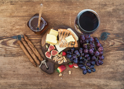 Glass of red wine  cheese board  grapes fig  strawberries  honey and bread sticks  on rustic wooden table