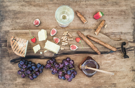 Glass of white wine  cheese board  grapes  figs  strawberries  honey and bread sticks on rustic wooden background