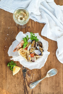 Seafood pasta  Spaghetti with clams and shrimps in bowl  glass of white wine over rustic wood background