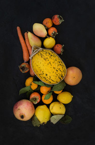 Mixed yellow orange fruit and veggies assortment  ingredients for smoothie  Melon  garnet  grapefruit  carrot  persimmon  lemon  quince  pear over black slate stone background
