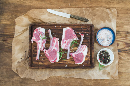 Rack of Lamb with rosemary and spices on rustic chopping board over oily craft paper  old wooden background
