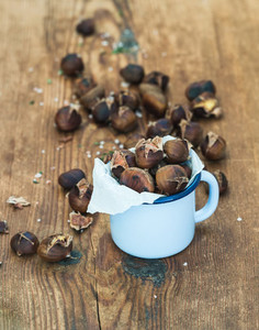 Roasted chestnuts in blue enamel mug on rustic wooden background  selective focus