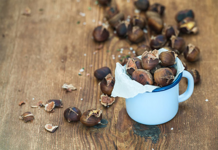 Roasted chestnuts in blue enamel mug on rustic wooden background selective focus