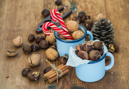 Traditional Christmas foods and decoration  Roasted chestnuts in blue  enamel mug  walnuts  cinnamon sticks  candy canes  pine cone on rustic wooden background
