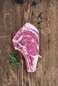 Raw fresh meat ribeye steak with pepper  salt and rosemary over rustic wooden background  top view