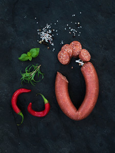 Smoked salami sausage with rosemary chili pepper basil and salt over black slate stone background top view closeup