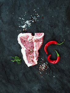 Raw fresh meat t bone steak with spices  chili peppers and rosemary over black slate stone background
