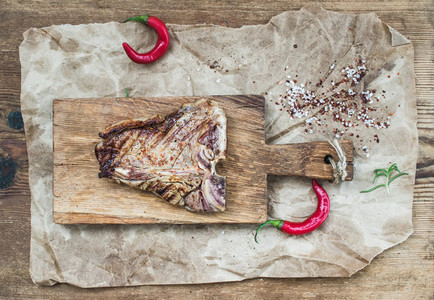 Cooked meat t bone steak on serving board with red chili peppers
