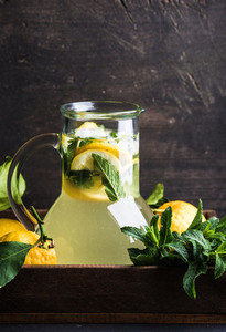 Homemade mint lemonade served with fresh lemons and ice over wooden background top view copy space