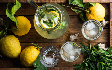 Homemade mint lemonade served with fresh lemons and ice over wooden background
