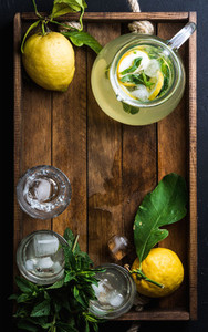 Homemade mint lemonade served with fresh lemons and ice over wooden background  top view  copy space