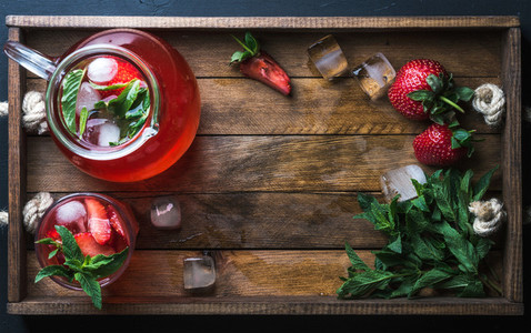 Homemade strawberry mint lemonade served with fresh berries and ice over wooden background top view copy space