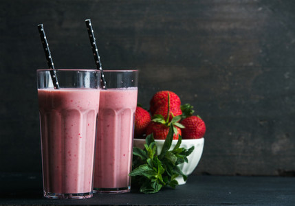 Strawberry and mint smoothie in tall glasses bawl of fresh berries on dark rustic wood background