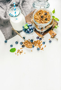 Healthy breakfast ingrediens  Homemade granola in open glass jar  milk or yogurt bottle  blueberries and mint