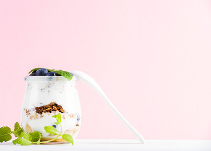 Yogurt oat granola with jam  blueberries and green leaves in glass jar on pink pastel backdrop