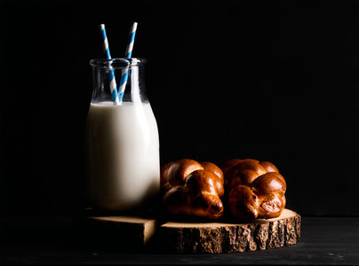 Bottle of milk and loaf buns on rustic wooden board over dark background