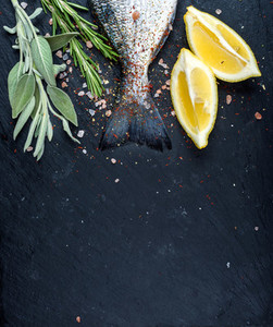 Tail of fresh raw Dorado or sea bream fish on black slate stone board with spices  herbs  lemon and salt