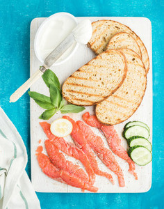 Ingredients for healthy sandwich  Grilled bread slices  smoked salmon  cottage cheese  cucumber and basil on white wooden board
