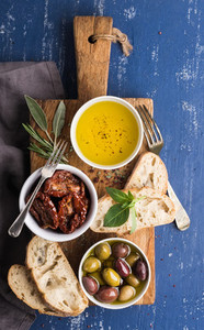 Mediterranean snacks set  Olives  oil  herbs and sliced ciabatta bread on yellow rustic oak board over painted dark blue background