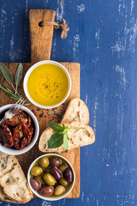 Mediterranean snacks set Olives oil herbs and sliced ciabatta bread on yellow rustic oak board over painted dark blue background