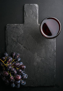 Glass of red wine and grapes on black slate stone board over dark background