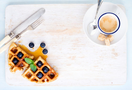Espresso coffee cup  soft belgian waffles with fresh blueberries and marple syrup on white painted wooden board over light blue background