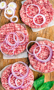 Raw ground beef meat cutlet for making burgers with onion rings and spices on wooden background