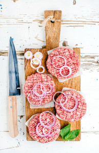 Raw ground beef meat cutlet for making burgers with onion rings and spices on wooden board over white backgroun