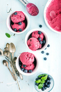 Homemade blueberry ice cream scoops with fresh berries and mint leaves in cups over light blue background