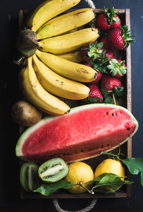 Various colorful tropical fruit selection in wooden tray over dark background