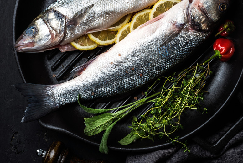Raw uncooked seabass fish with herbs and spices in cast iron cooking pan on black wooden background