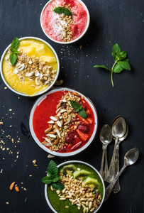 Healthy summer breakfast concept  Colorful fruit smoothie bowls with nuts and oat granola on black background