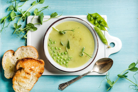 Light summer green pea cream soup in bowl with sprouts bread toasts and spices