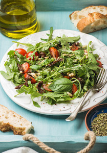 Salad with arugula cherry tomatoes pine nuts and herbs on white ceramic plate over blue wood background