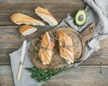 Salmon avocado and thyme sandwiches in baguette tied up with decoration rope on a rustic wooden board over rough wood background