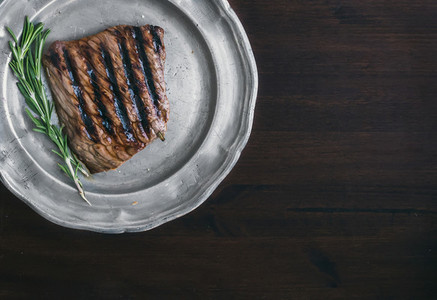 Beef steak with rosemary on a vintage metal plate over a dark wo