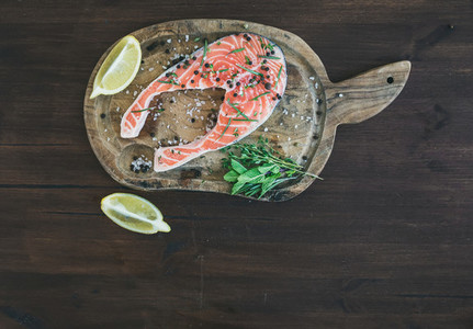 Raw salmon steak with fresh herbs lemon and spices on rustic wo